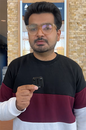 Man in glasses holding a small black object indoors.