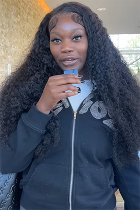 Woman with long curly hair holding a phone, wearing a black jacket.