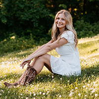 Woman in a white dress sitting on grass, smiling.