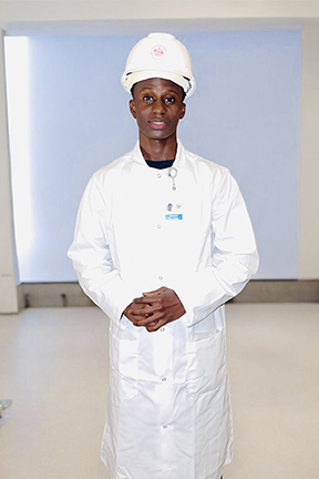 Man in a white coat and helmet standing indoors.