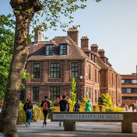 Students walking past the welcome sign and the red-brick campus buildings