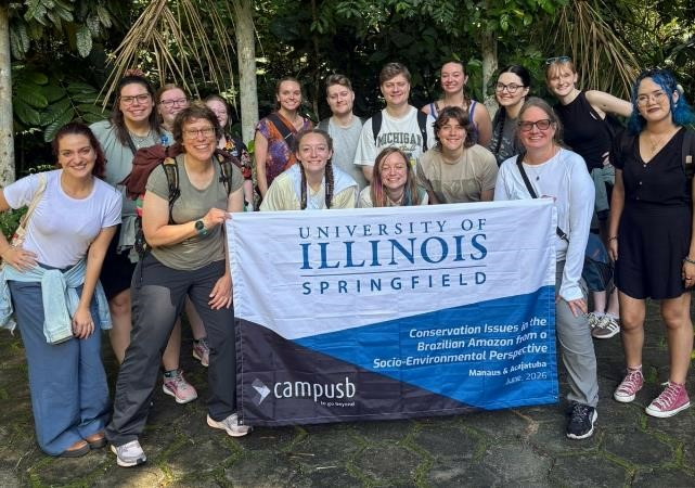 Study away students in Brazil around UIS banner with professors Amy McEuen and Megan Styles.
