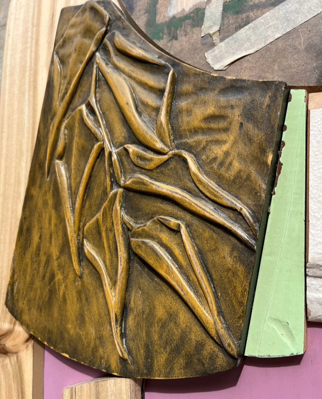 Relief sculpture by Jeff Robinson with layered, folded abstract forms in bronze and black, creating a textured, organic composition on a curved panel.