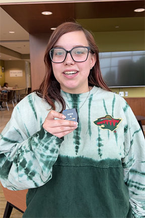 Young person in glasses with sweater, holding a small object indoors, smiling.