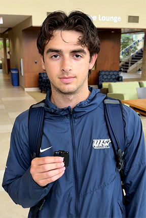 Young man in a blue tracksuit holds a small object in a lounge area.