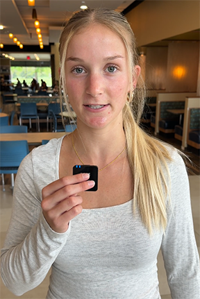 Young woman in a casual setting, holding a small black object, wooden decor in background.