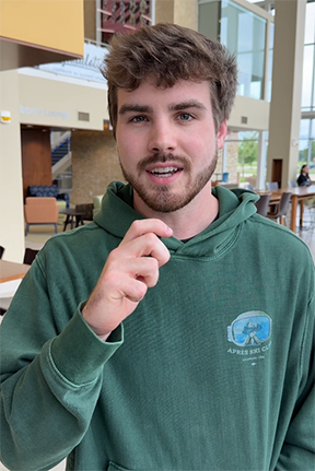 Young man in a green hoodie indoors, holding a small object.