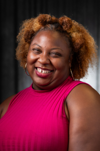 Smiling woman in a red top against a dark background.