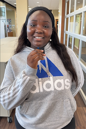 Smiling woman in a gray hoodie stands indoors.