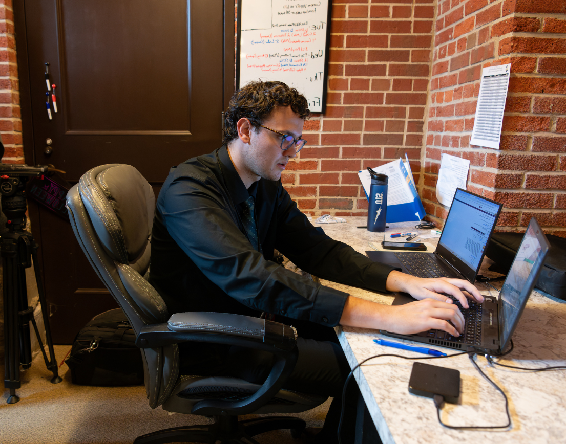 A man typing on a computer in a red brick office.