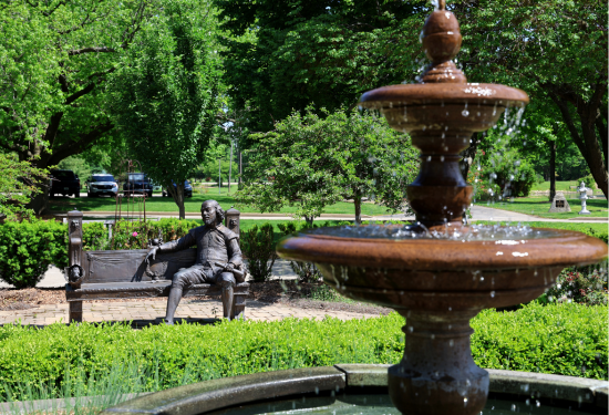 Fountain and bench with statues in a lush green park.