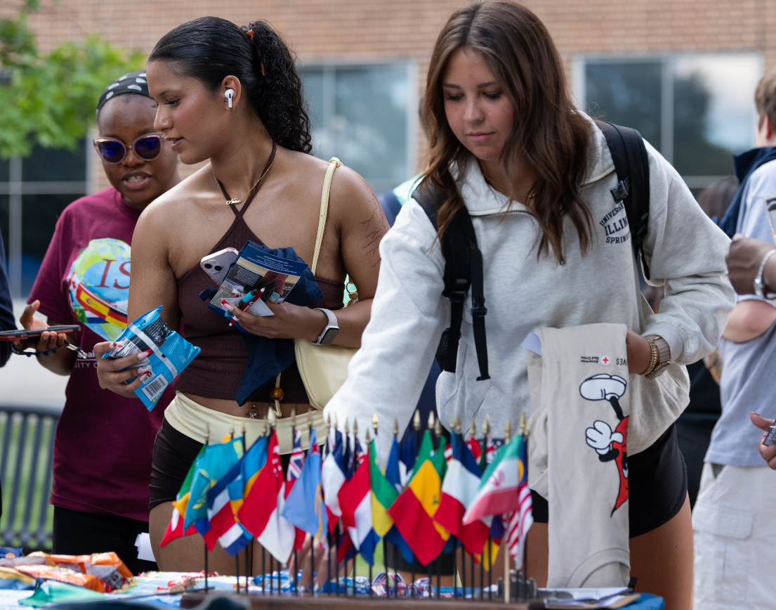Two women reach for items on a table covered with flags.