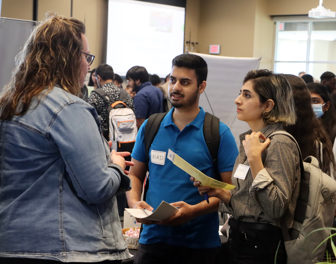 Two people listen intently to an employer at a busy job fair.