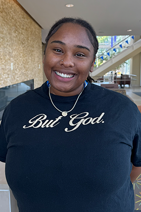 Female student wearing a black "But God" t-shirt indoors.