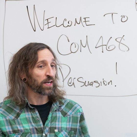 a Communications professor standing in front of a white board