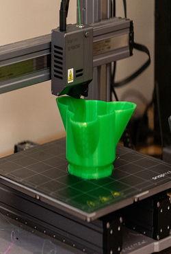 A 3D printer printing a green three petal dish at the Orion Lab at the University of Illinois Springfield