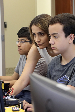 Elham Buxton (center) is shown reaching past a student to control a computer during an AI summer camp.