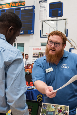 A man holds a piece of paper while talking to a student about a job.