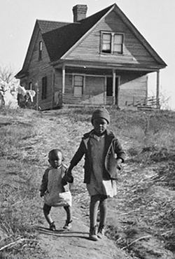 A black and white photo showing a house on top of a hill with two children, one with Rickets, walking towards the camera. 