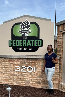 UIS student Wonder Odutola stands next to Federated Fiducial sign.