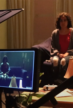 A camera and screen and shown capturing an image of a girl sitting on a couch.