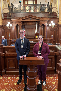 Two students pose on the floor of the Illinois State Senate.