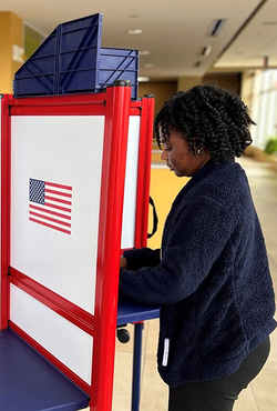 Student casts ballot at a red, white and blue voting booth inside the University of Illinois Springfield student union.