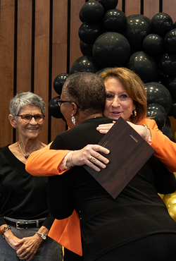 A person receives an award and a hug during the Good as Gold Volunteer Awards ceremony, with others smiling nearby.