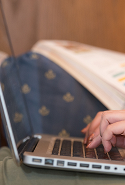 Close-up of a person typing on a laptop with an open textbook in the background.