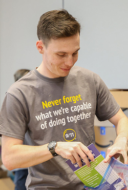 A person packing a colorful bag with supplies in a room filled with boxes. Their shirt reads, "Never forget what we're capable of doing together." 