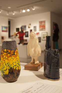 Art gallery with colorful vase, sculpture, and dark vase on display.