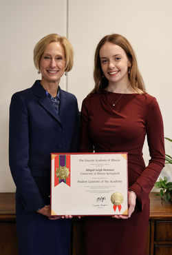 Two women smiling with an award certificate in a professional setting.