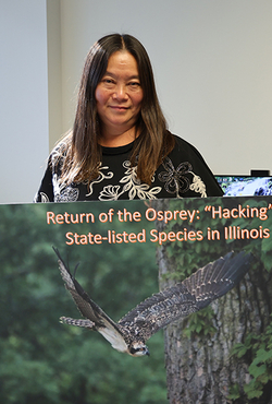 A woman standing, holding a large poster of an osprey in flight.