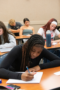 Students focused on writing at desks in a classroom.