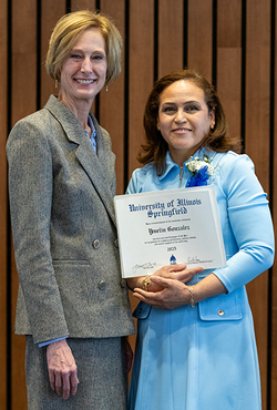 Two women smiling, one holding a certificate, standing indoors.