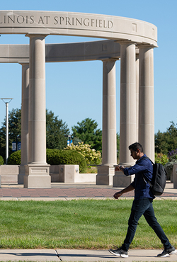 Person walking past a circular column structure with a clear blue sky.