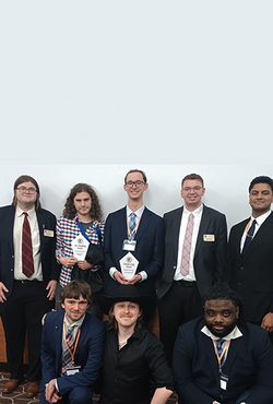 Eight people in formal attire, two holding awards, smiling indoors.