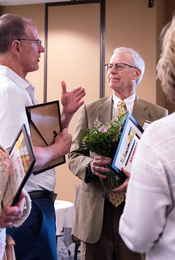 Two men in discussion at an event, holding framed certificates.