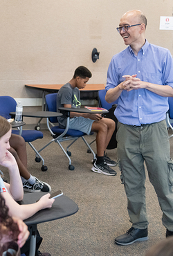 Man in blue shirt speaking to students in a classroom setting.