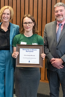 Three people standing, one holding a framed certificate.