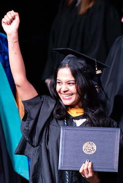 Graduate smiling, holding diploma, raising fist on stage.
