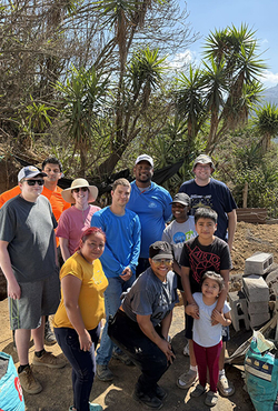 Group of people posing outdoors with trees and mountains in the background.