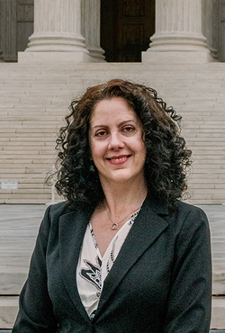 Woman in a suit smiling in front of a building with large steps.