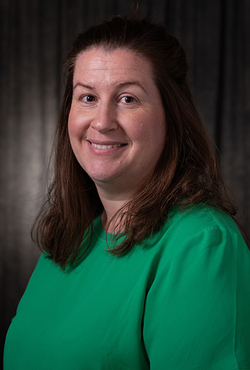 Smiling woman in a green shirt against a dark background.