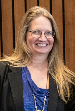 Smiling woman with long hair, wearing glasses and a blue top.