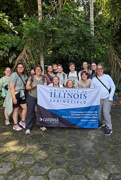 Group of people holding a University of Illinois Springfield banner in a lush, green setting.