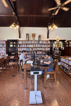 Cozy library with two people working at a wooden table, surrounded by bookshelves.