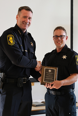 Two uniformed officers smiling as one receives a plaque.
