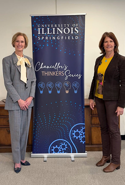 Two women standing beside University of Illinois Springfield banner indoors.