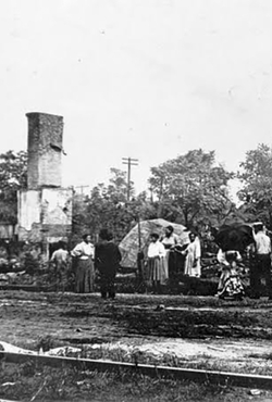 People standing near a tall, damaged building with trees in the background.